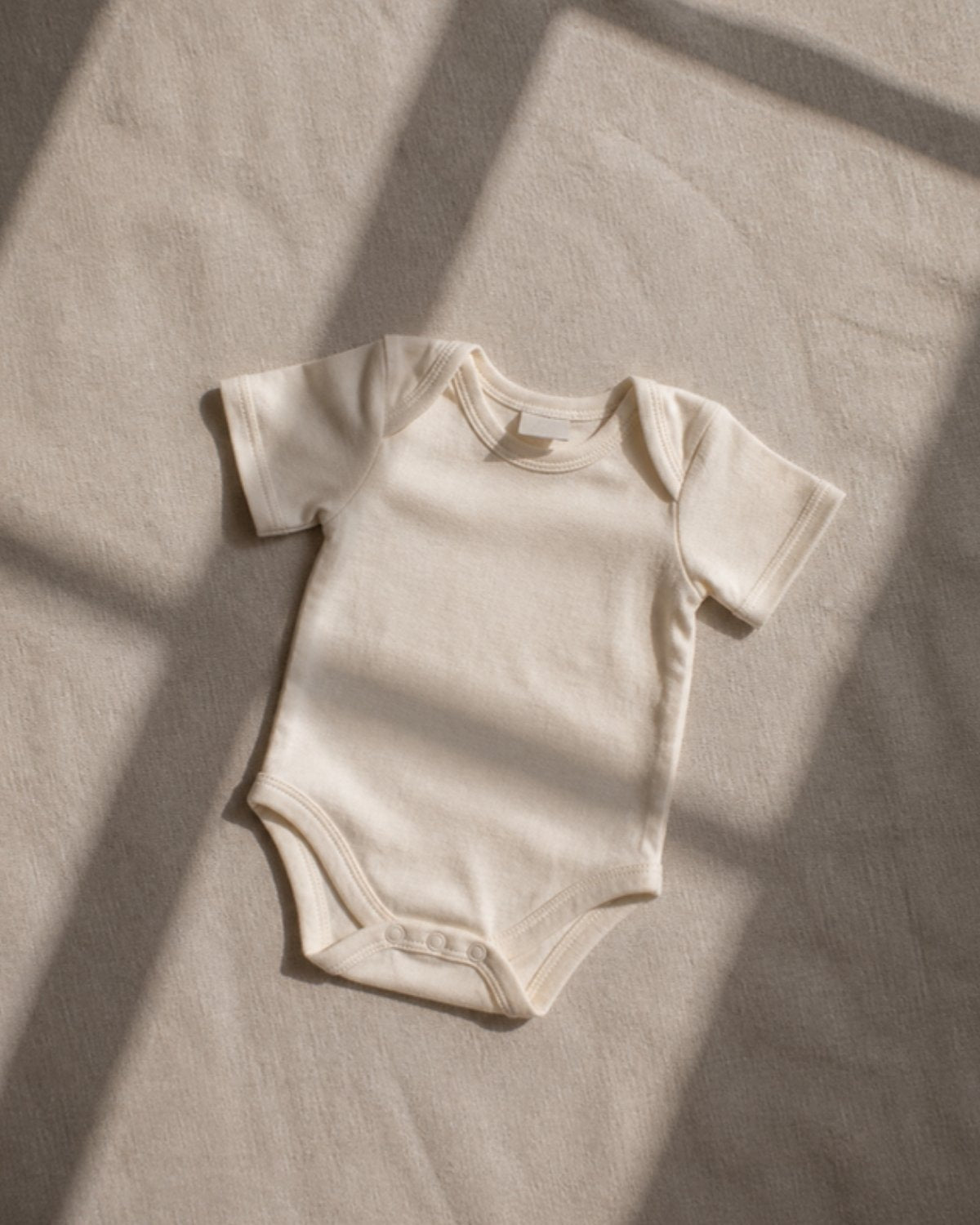 An undyed organic cotton baby bodysuit on linen with its care label turned outward